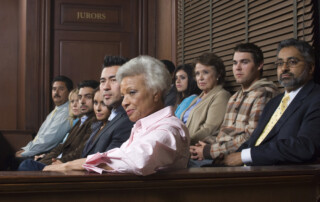 In a courtroom, a white-haired man in a pink shirt sits at the front with jurors behind him.