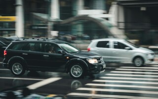 Black SUV and silver car moving through a busy urban crosswalk intersection.