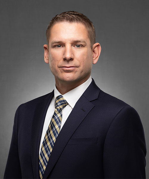 Portrait of a man in a navy suit and striped tie, posing against a grey studio background.