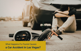 Person sitting on the ground beside a damaged car, with a spare wheel lying nearby after a crash.